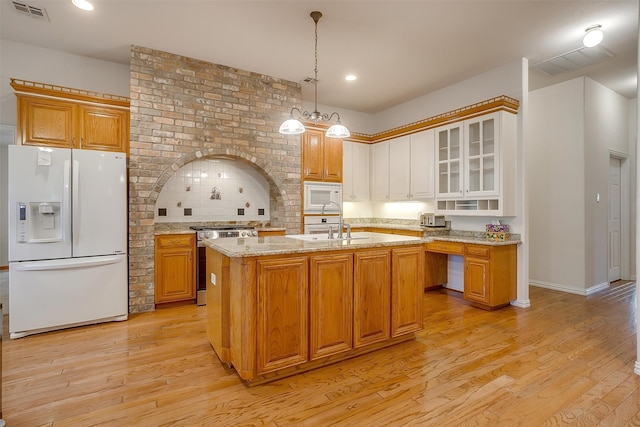 kitchen featuring light wood-type flooring, decorative light fixtures, light stone countertops, an island with sink, and white appliances