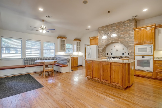 kitchen with light hardwood / wood-style floors, an island with sink, pendant lighting, breakfast area, and white appliances