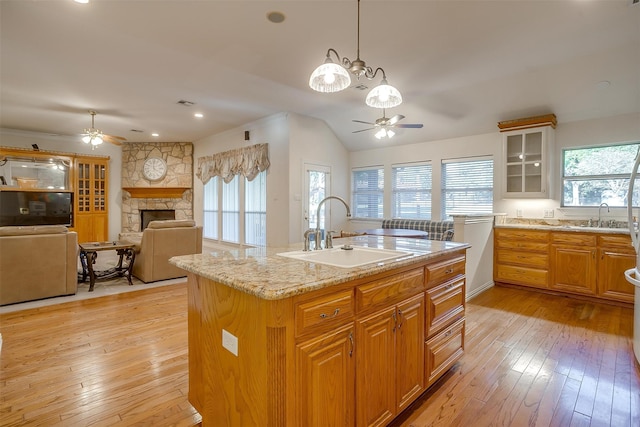 kitchen with light hardwood / wood-style floors, sink, white dishwasher, a stone fireplace, and a kitchen island with sink