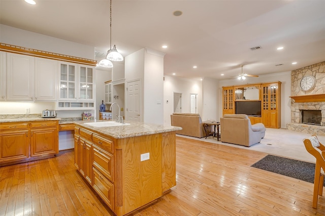 kitchen featuring a kitchen island with sink, a fireplace, pendant lighting, sink, and light hardwood / wood-style flooring