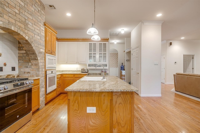 kitchen with a kitchen island with sink, stainless steel gas stove, white microwave, light hardwood / wood-style flooring, and wall oven