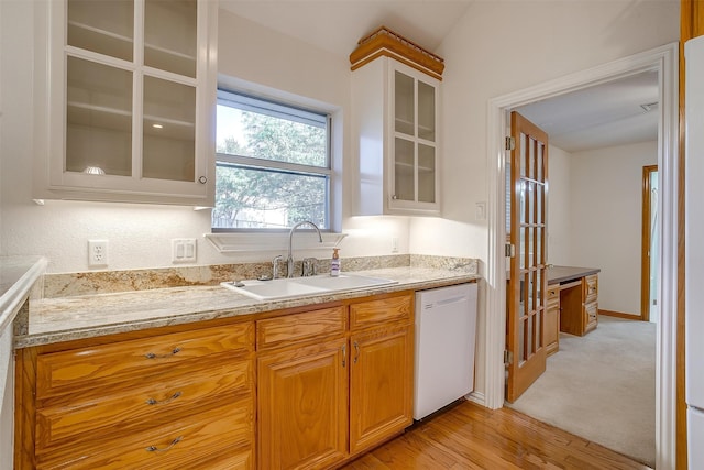 kitchen featuring white dishwasher, sink, light wood-type flooring, and light stone counters