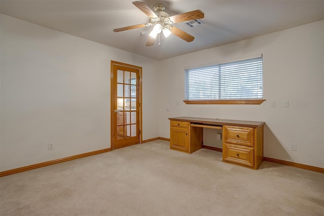 unfurnished office with built in desk, ceiling fan, and light carpet