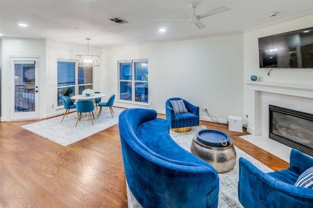 living room featuring crown molding, ceiling fan with notable chandelier, light hardwood / wood-style floors, and a fireplace