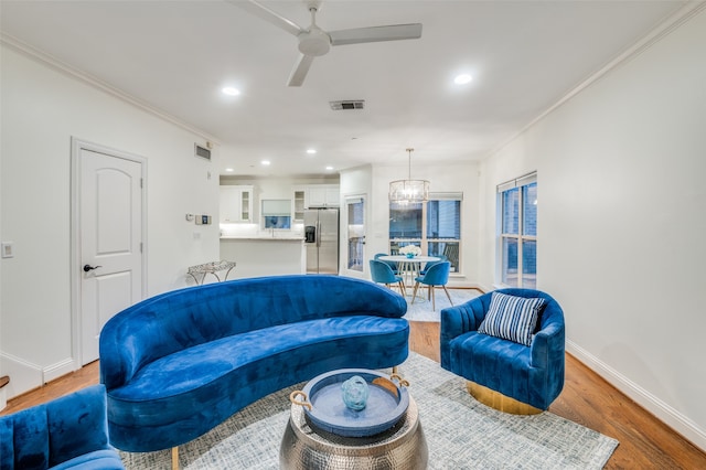 living room featuring hardwood / wood-style floors, ceiling fan with notable chandelier, and ornamental molding