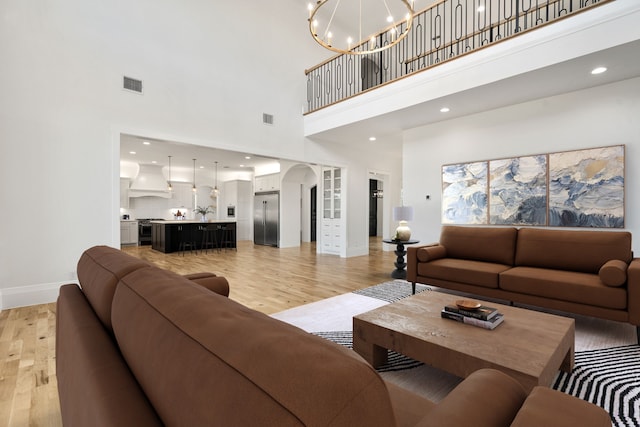 living room with a towering ceiling, a chandelier, and light wood-type flooring