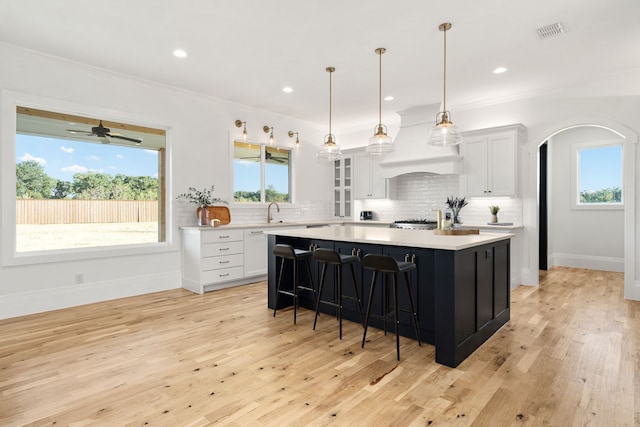 kitchen featuring light hardwood / wood-style floors, a center island, crown molding, white cabinetry, and premium range hood