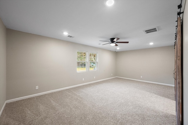 unfurnished room with a barn door, ceiling fan, and carpet flooring