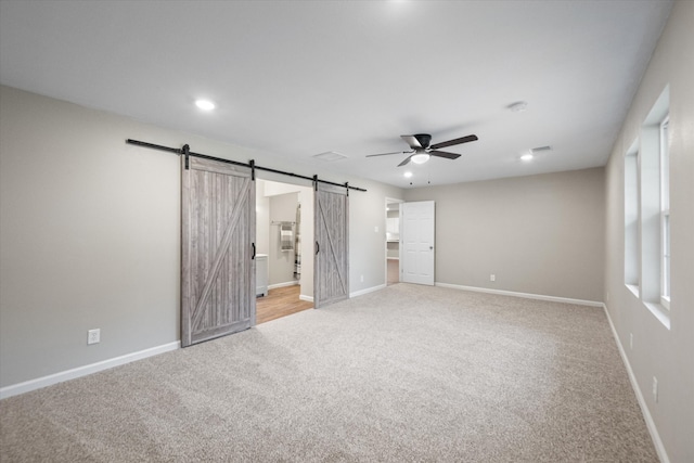 unfurnished bedroom with ensuite bathroom, light carpet, a barn door, and ceiling fan