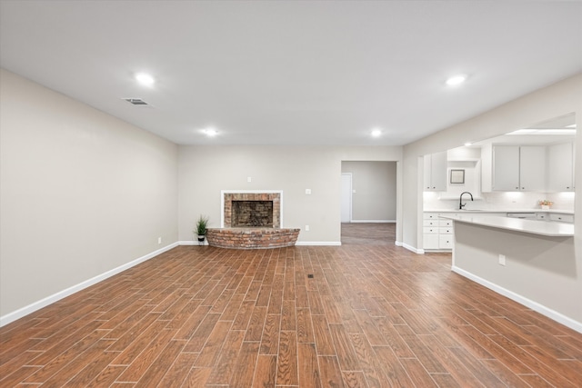 unfurnished living room with sink, hardwood / wood-style floors, and a brick fireplace