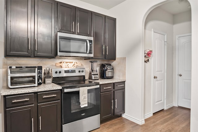 kitchen featuring stainless steel appliances, backsplash, dark brown cabinetry, and light wood-type flooring