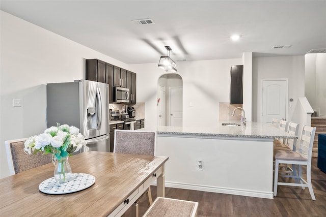 kitchen with sink, kitchen peninsula, appliances with stainless steel finishes, light stone countertops, and dark hardwood / wood-style floors