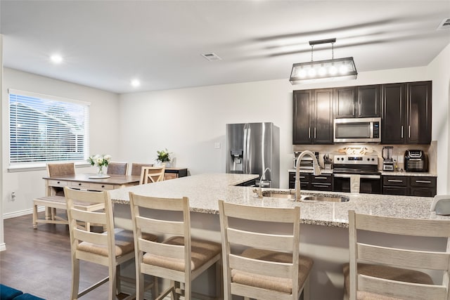 kitchen with a center island with sink, appliances with stainless steel finishes, a kitchen bar, dark brown cabinets, and sink