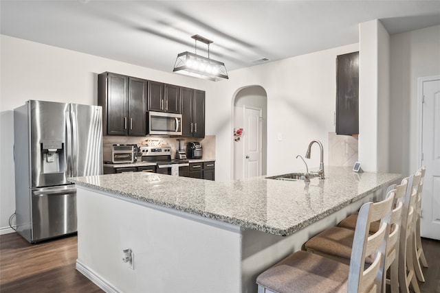 kitchen with light stone counters, appliances with stainless steel finishes, dark hardwood / wood-style floors, hanging light fixtures, and sink