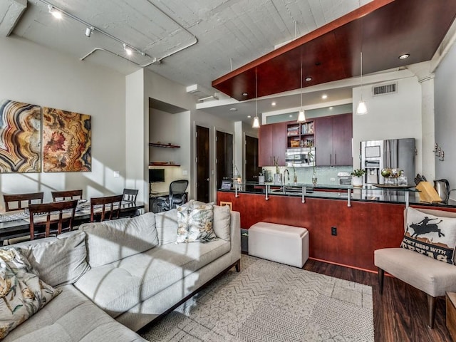 interior space featuring appliances with stainless steel finishes, tasteful backsplash, track lighting, hardwood / wood-style floors, and hanging light fixtures