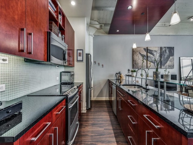 kitchen with sink, dark wood-type flooring, dark stone countertops, pendant lighting, and appliances with stainless steel finishes