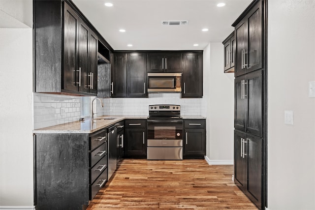 kitchen featuring light hardwood / wood-style floors, sink, light stone counters, appliances with stainless steel finishes, and decorative backsplash