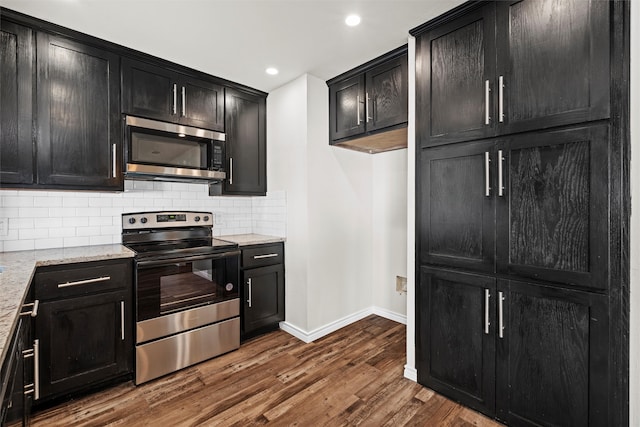 kitchen featuring dark hardwood / wood-style flooring, light stone counters, appliances with stainless steel finishes, and tasteful backsplash