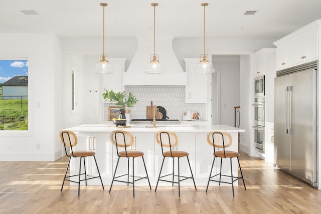 kitchen featuring built in appliances, decorative backsplash, white cabinets, light hardwood / wood-style flooring, and decorative light fixtures