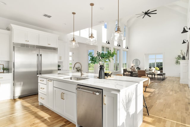 kitchen with white cabinets, appliances with stainless steel finishes, a kitchen island with sink, and sink