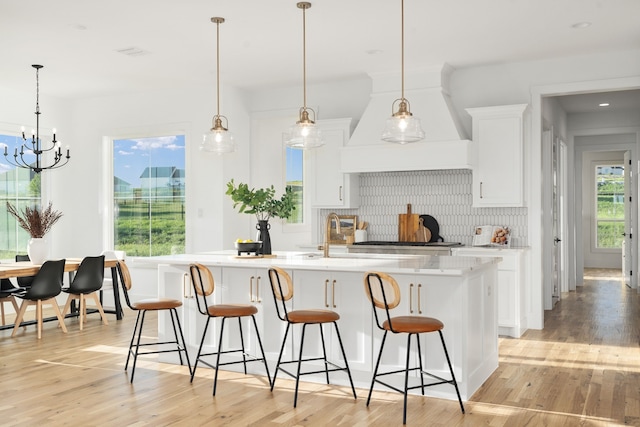 kitchen with white cabinetry, light wood-type flooring, hanging light fixtures, and an island with sink