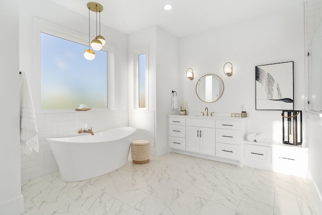 bathroom with a tub to relax in, vanity, and tile walls