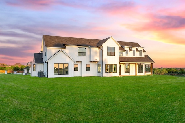 back house at dusk with a lawn and cooling unit