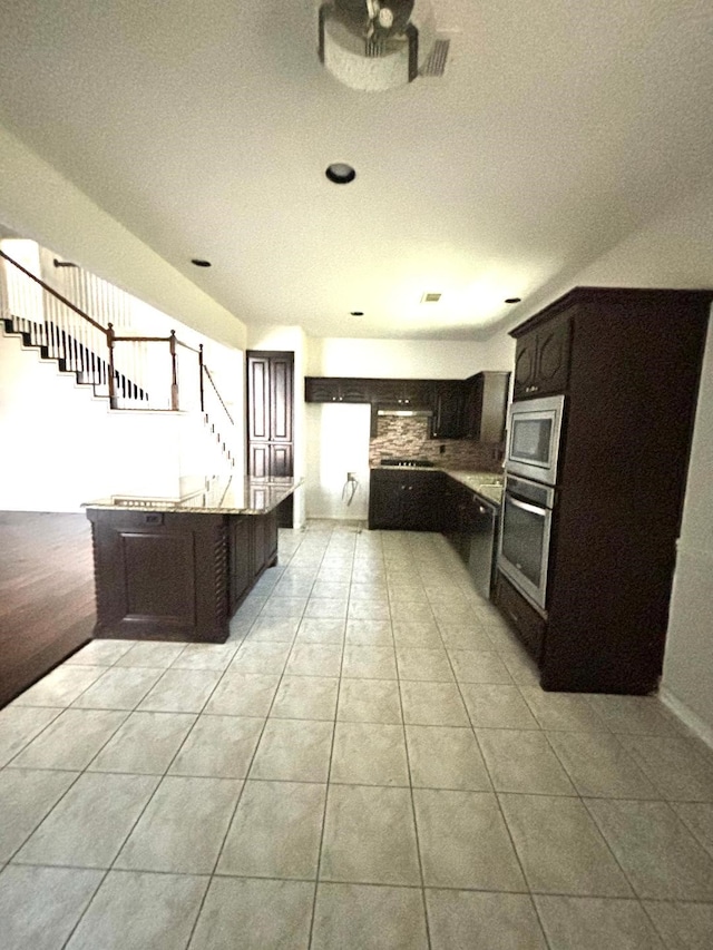 kitchen featuring dark brown cabinets, a kitchen bar, stainless steel appliances, and light tile patterned floors