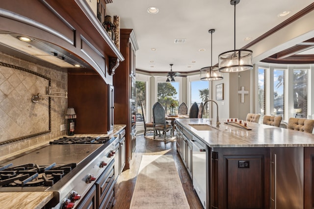 kitchen featuring decorative light fixtures, dark brown cabinetry, sink, and an island with sink