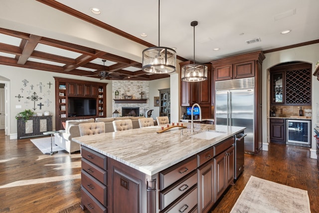 kitchen with pendant lighting, coffered ceiling, a stone fireplace, an island with sink, and beamed ceiling