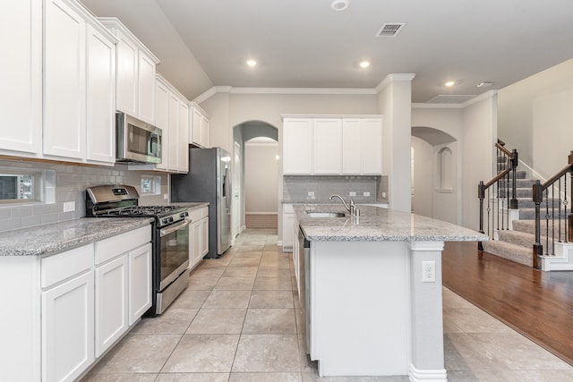 kitchen with appliances with stainless steel finishes, decorative backsplash, an island with sink, and white cabinets