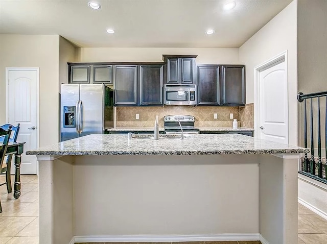 kitchen featuring a kitchen island with sink, decorative backsplash, appliances with stainless steel finishes, and light stone counters