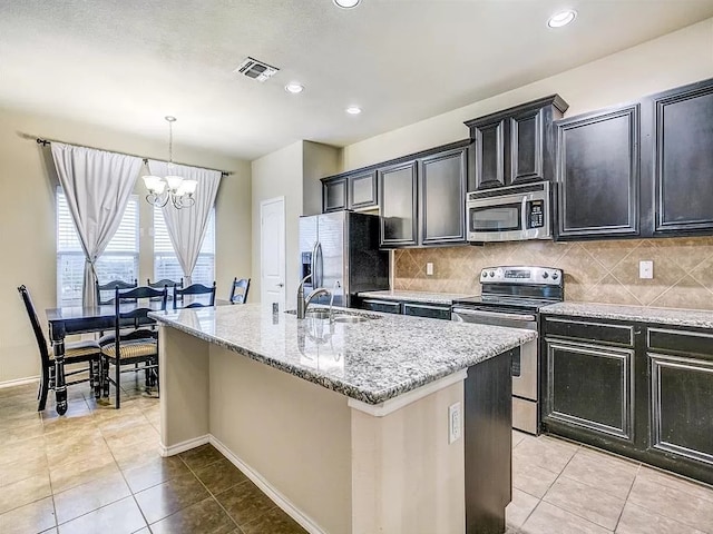 kitchen with a notable chandelier, an island with sink, backsplash, appliances with stainless steel finishes, and decorative light fixtures