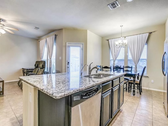 kitchen with stainless steel appliances, hanging light fixtures, sink, an island with sink, and light stone countertops