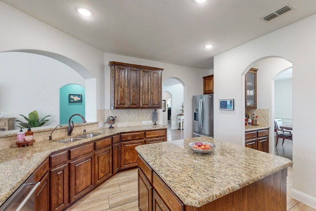 kitchen with tasteful backsplash, light stone counters, stainless steel appliances, sink, and a center island