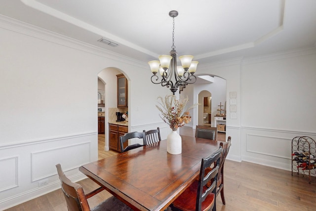 dining room with a chandelier, a raised ceiling, light hardwood / wood-style flooring, and crown molding