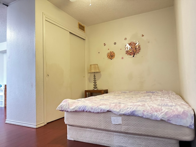 bedroom with dark hardwood / wood-style floors, a textured ceiling, and a closet