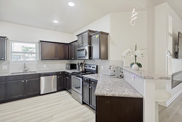 kitchen with light hardwood / wood-style floors, sink, light stone counters, appliances with stainless steel finishes, and hanging light fixtures