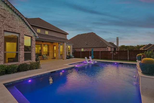 pool at dusk with pool water feature and a patio