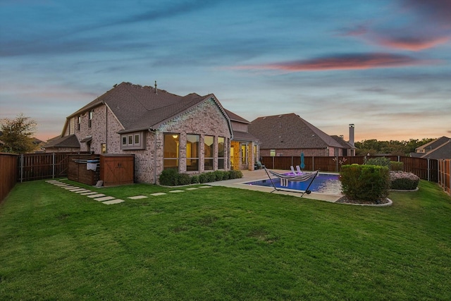 back house at dusk featuring an outdoor kitchen, a fenced in pool, and a yard