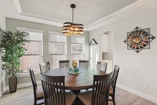 dining space featuring ornamental molding, a tray ceiling, a notable chandelier, and light hardwood / wood-style floors