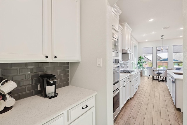 kitchen featuring decorative backsplash, appliances with stainless steel finishes, decorative light fixtures, light stone counters, and white cabinetry