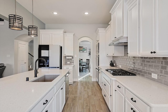 kitchen with sink, hanging light fixtures, light stone countertops, white cabinetry, and stainless steel appliances