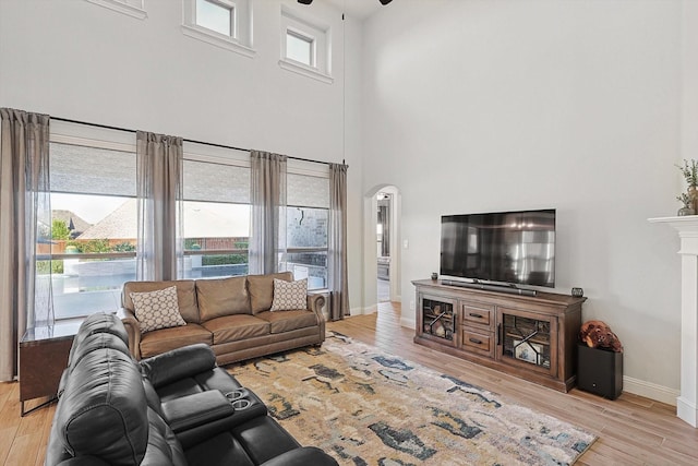 living room featuring ceiling fan, plenty of natural light, a high ceiling, and light wood-type flooring