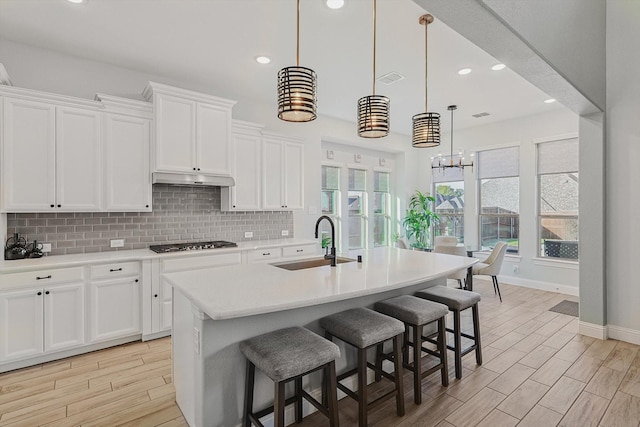 kitchen featuring white cabinetry, sink, hanging light fixtures, stainless steel gas stovetop, and a center island with sink