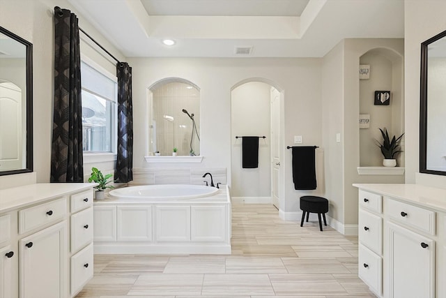 bathroom with vanity, a tub, and a tray ceiling