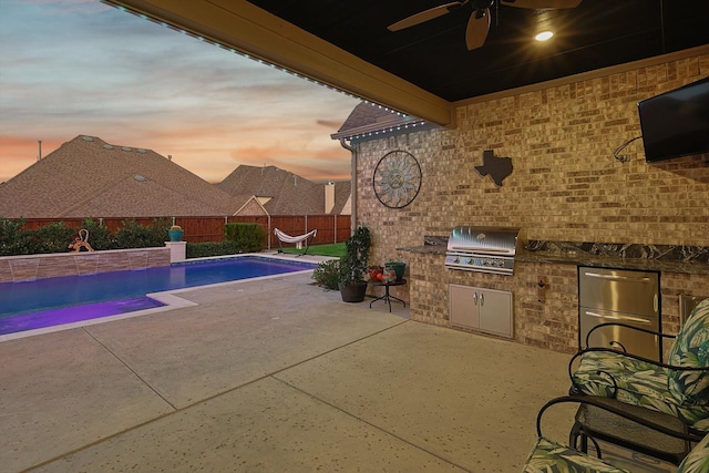 pool at dusk with a grill and exterior kitchen