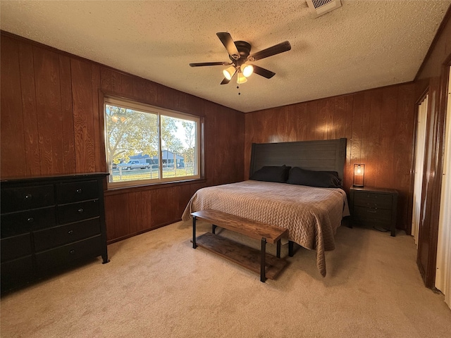 bedroom featuring ceiling fan, wood walls, light carpet, and a textured ceiling