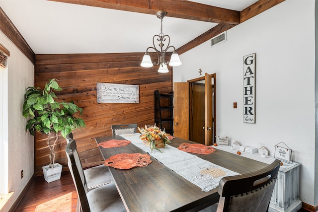 dining space featuring dark wood-type flooring, wooden walls, beam ceiling, and an inviting chandelier