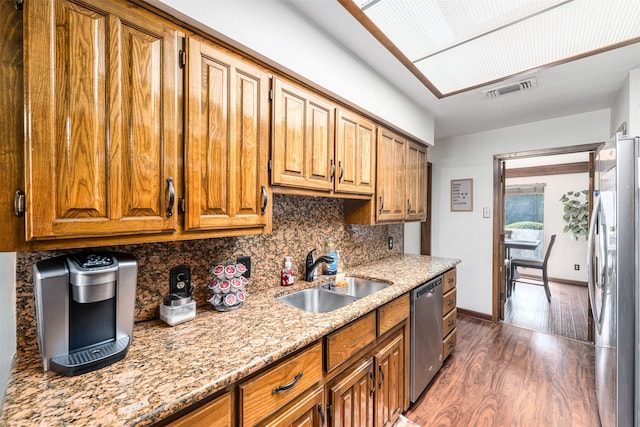 kitchen with stainless steel appliances, dark hardwood / wood-style flooring, decorative backsplash, sink, and light stone countertops